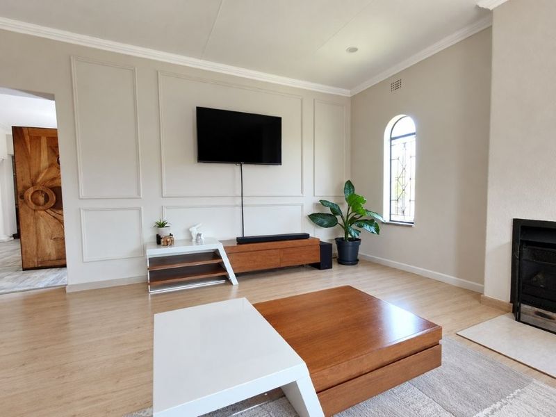 A well-maintained living room featuring elegant wainscoting, an arched window, and a fireplace, finished with light-toned laminate flooring and crown molding.