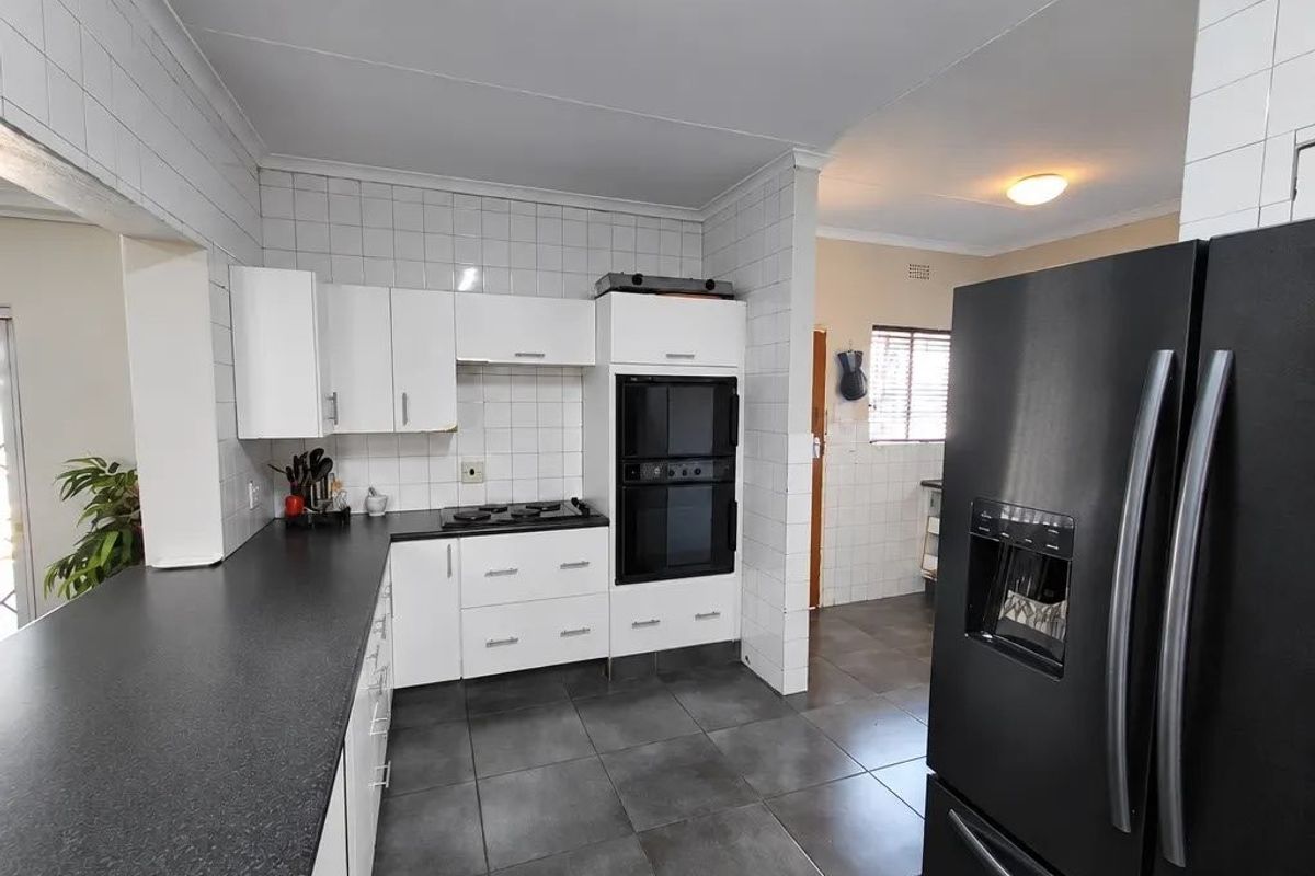 A functional kitchen featuring white cabinetry, dark countertops, a built-in double oven, gas hob, and tiled flooring throughout.