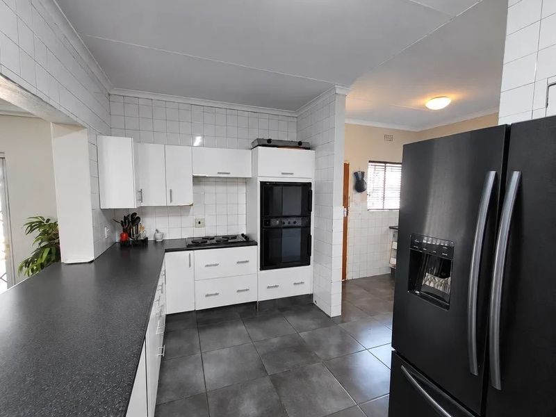 A functional kitchen featuring white cabinetry, dark countertops, a built-in double oven, gas hob, and tiled flooring throughout.