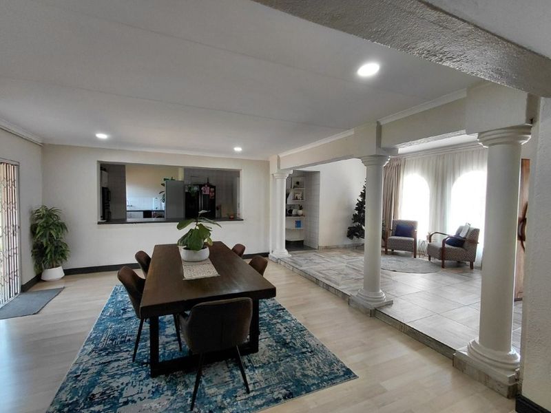 Spacious open-plan living and dining area featuring decorative columns, a mix of tiled and laminate flooring, and a convenient pass-through window to the kitchen.