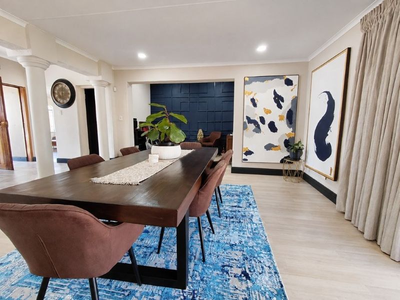 A spacious dining room featuring decorative columns, modern recessed lighting, and a feature wall with wainscoting, finished with light-toned laminate flooring.