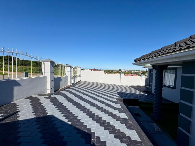 A well-maintained front exterior featuring a patterned paved driveway, perimeter wall with metal fencing, and a decorative pillar under a tiled roof.