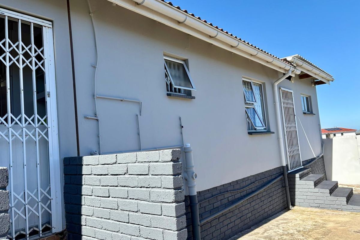 Rear exterior view of the house featuring a brick plinth, security gates, and aluminium window frames under a tiled roof.