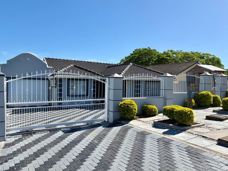 Front elevation of a well-maintained house featuring a paved driveway, secure perimeter wall with metal gate, and a tiled roof.