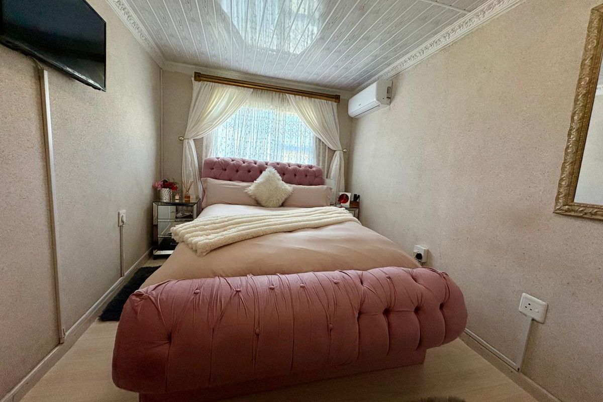 A compact bedroom featuring laminate flooring, a textured ceiling with coving, and a wall-mounted air conditioning unit.