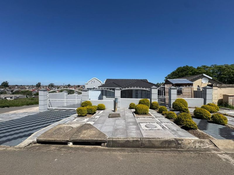 Front exterior view of the property featuring a paved driveway, boundary wall with metal gates, and a landscaped front garden area.