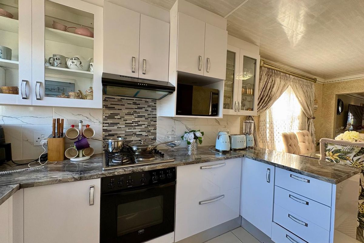 A well-maintained kitchen featuring white cabinetry, stone-look countertops, a gas hob with extractor fan, and a tiled backsplash.