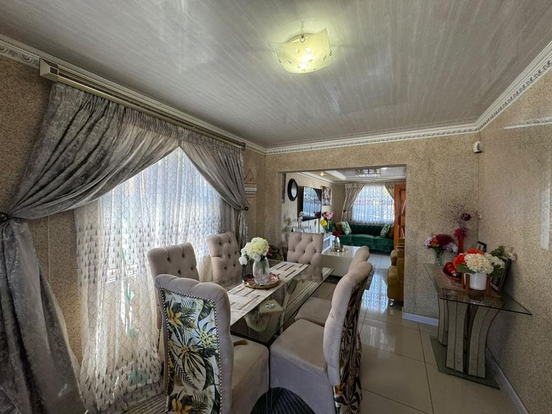 Dining room featuring tiled flooring, decorative ceiling cornices, and a wall-mounted air conditioning unit, with an open-plan flow into the adjacent living area.