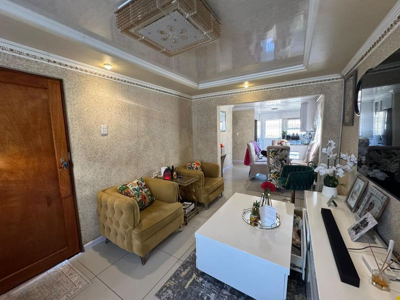 Open plan living area featuring tiled floors, decorative ceiling moulding, and textured wallpaper, with a seamless transition into the adjacent dining and kitchen space.