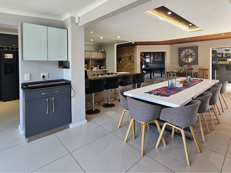 Spacious open-plan living and dining area featuring modern cabinetry, a kitchen island with hob, tiled floors, and a stylish timber ceiling detail.