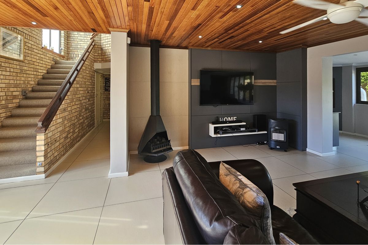 Spacious living room featuring a striking timber ceiling, exposed brick wall, staircase, and a modern built-in media wall with a freestanding fireplace.