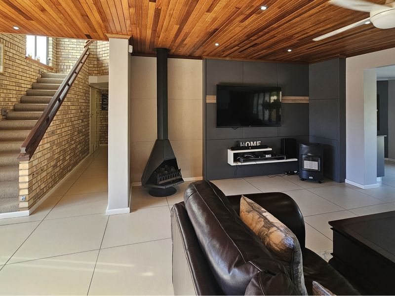 Spacious living room featuring a striking timber ceiling, exposed brick wall, staircase, and a modern built-in media wall with a freestanding fireplace.