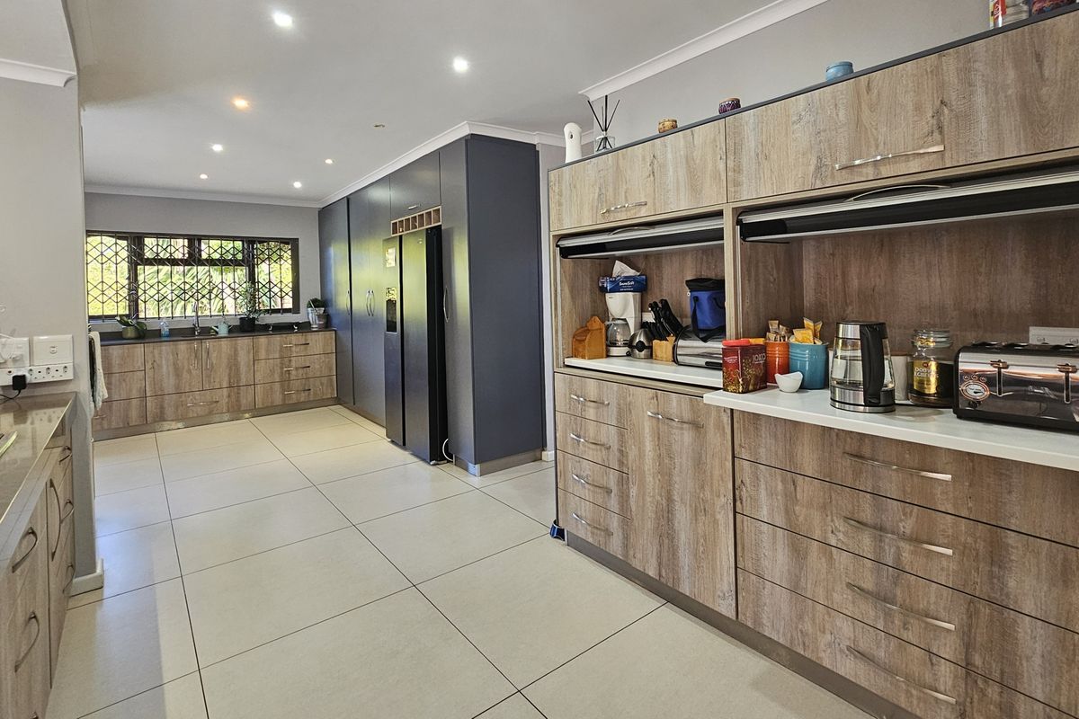 Modern kitchen featuring extensive wood-grain cabinetry, stone countertops, integrated appliances, recessed lighting, and large format floor tiles.