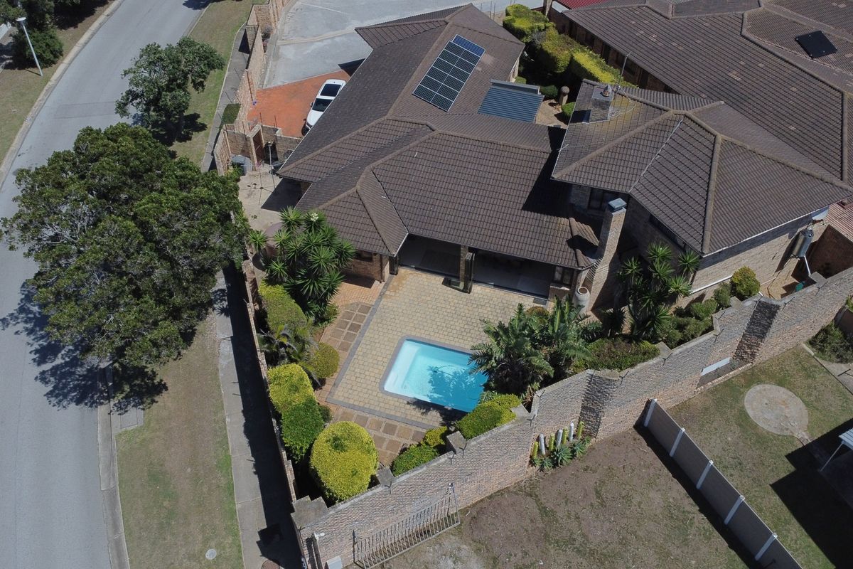 Aerial view of a residential property featuring a tiled roof with solar panels, a private swimming pool, and a paved patio area.