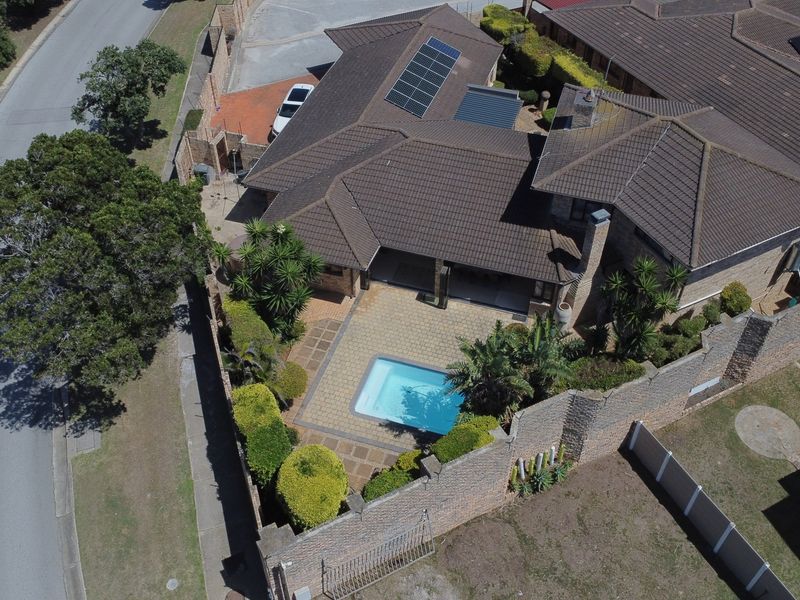 Aerial view of a residential property featuring a tiled roof with solar panels, a private swimming pool, and a paved patio area.