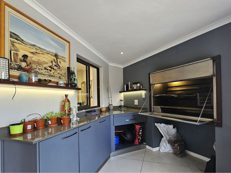 Indoor entertainment area featuring a built-in braai, modern cabinetry with stone countertops, and tiled flooring, perfect for hosting and dining.
