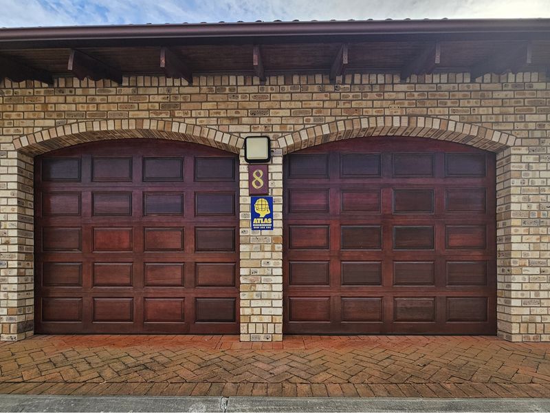 A well-maintained double garage featuring classic timber doors, brick masonry, and paved driveway access.