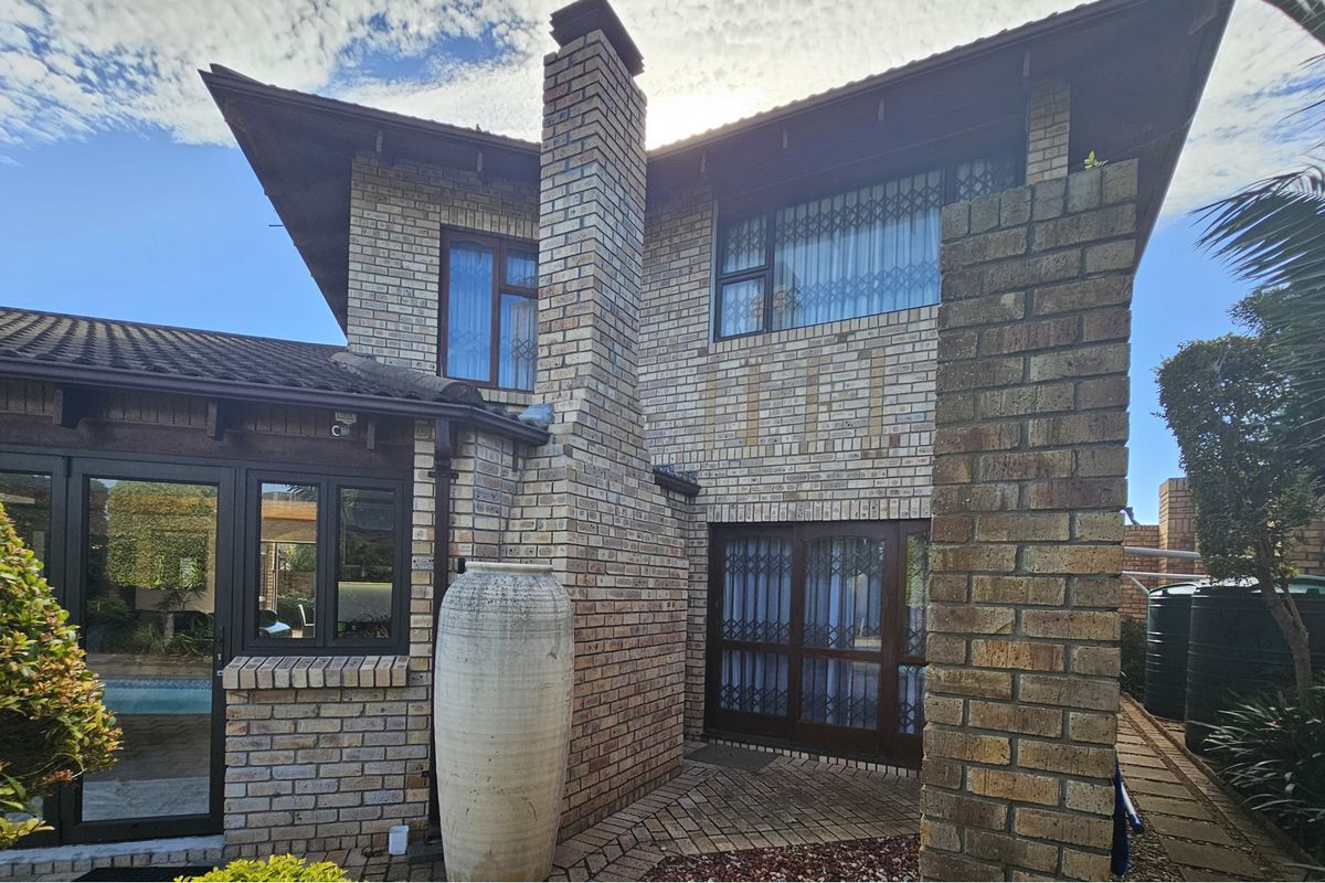 Rear exterior view of a face brick house featuring a prominent chimney, paved patio area, and integrated security gates on windows and doors.