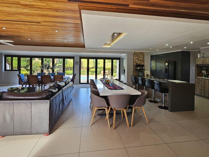 Spacious open-plan living, dining, and kitchen area featuring a timber ceiling, modern cabinetry, kitchen island, and large bi-fold doors opening to the garden.