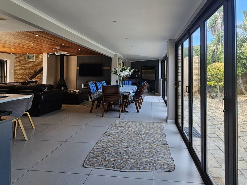 Spacious open-plan living and dining area featuring large format floor tiles, a timber slat ceiling, and expansive sliding glass doors opening to the patio.