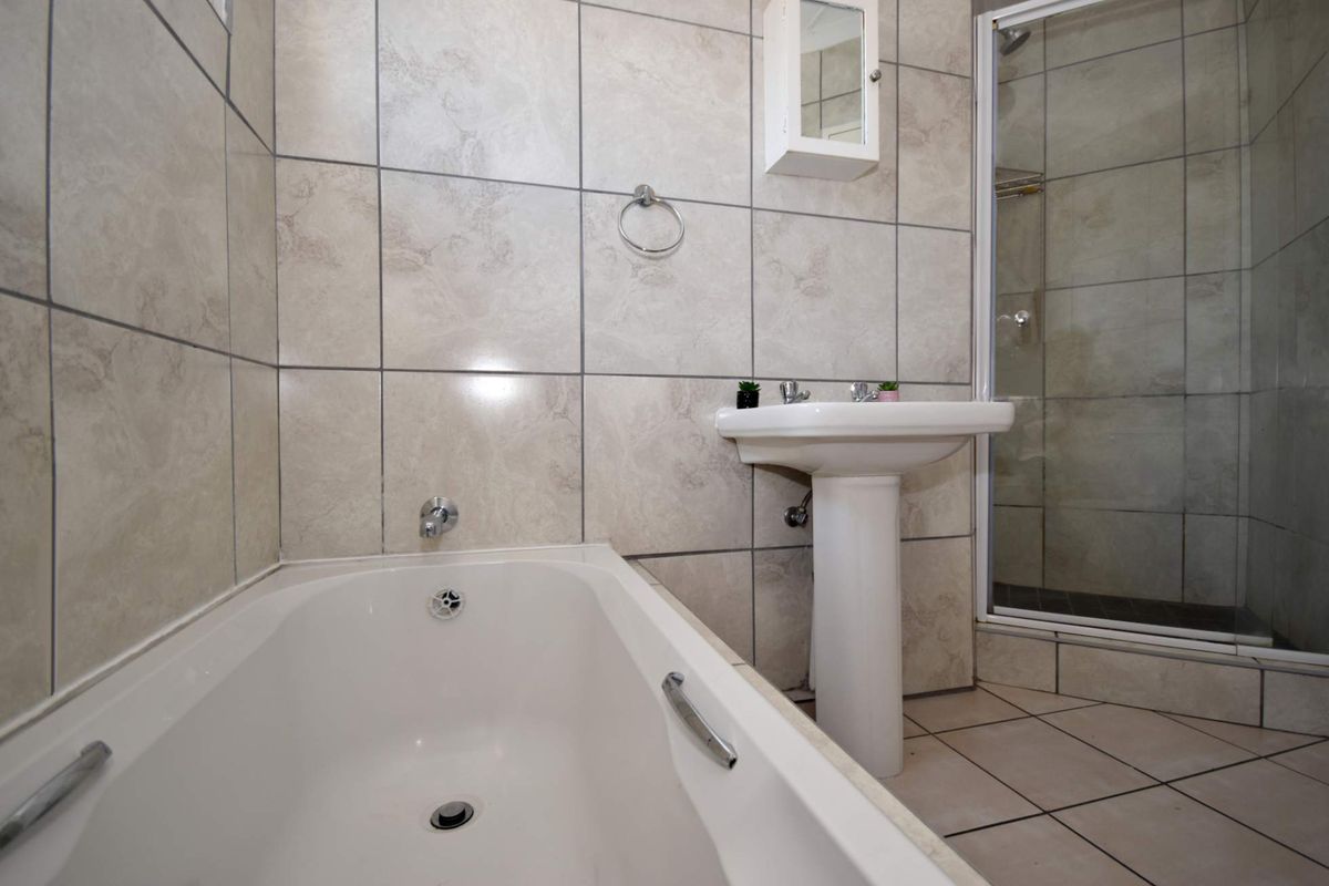 A functional bathroom featuring a pedestal basin, a built-in bathtub, and a separate shower enclosure with neutral wall and floor tiling.