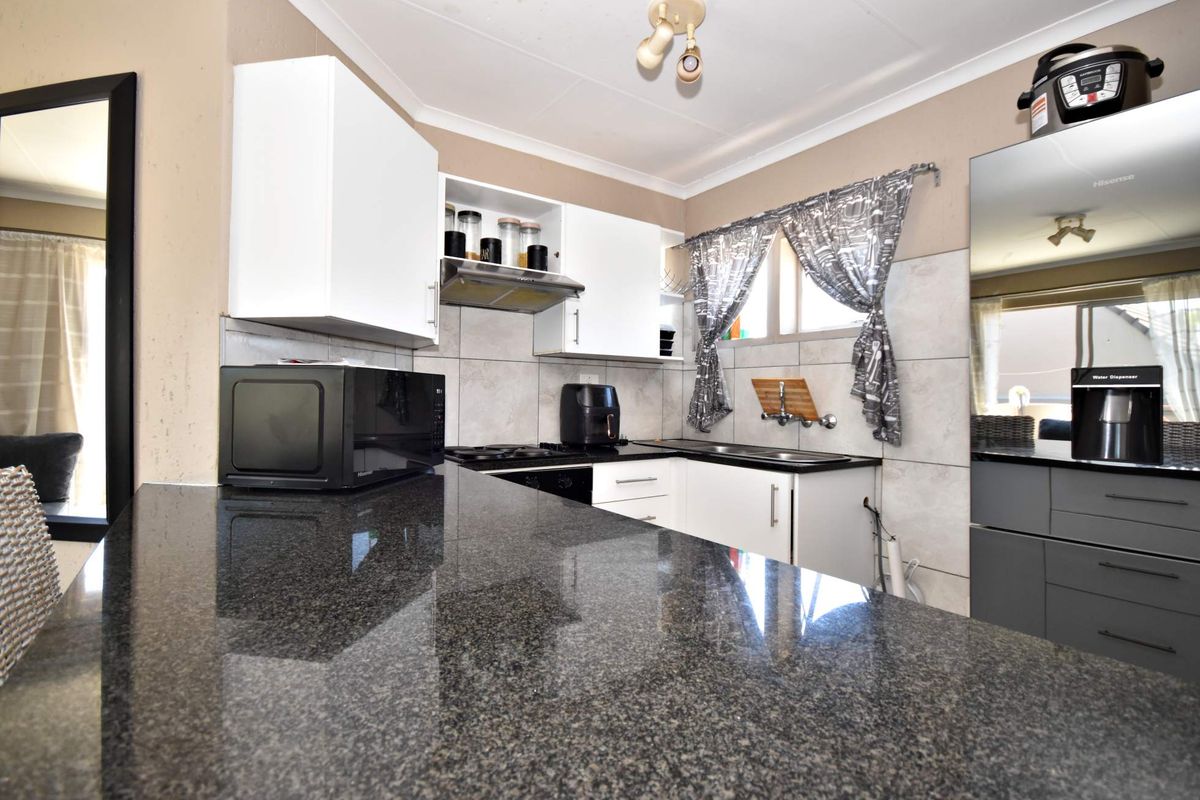 A functional kitchen featuring granite countertops, white cabinetry, a built-in hob with extractor fan, and a tiled backsplash.