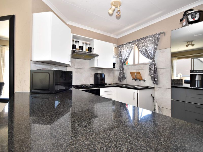 A functional kitchen featuring granite countertops, white cabinetry, a built-in hob with extractor fan, and a tiled backsplash.