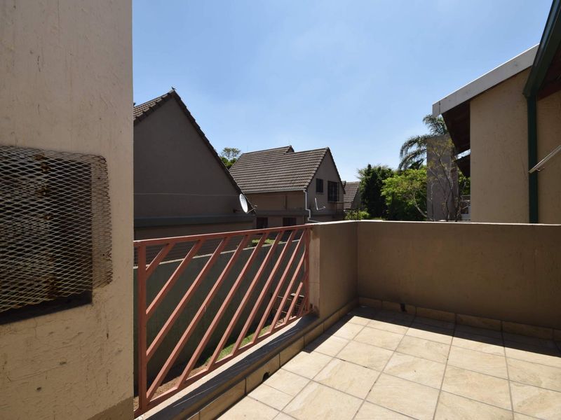 An open-air balcony featuring tiled flooring and a metal balustrade, offering a functional outdoor space with views of the surrounding residential complex.