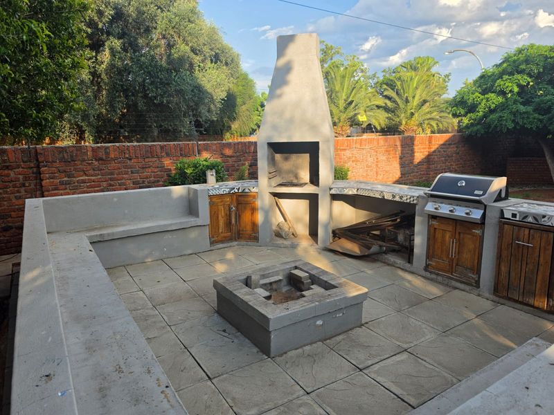Outdoor entertainment area featuring a built-in braai, central fire pit, integrated concrete seating, and built-in cabinetry, set within a private garden space.