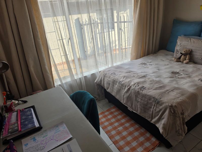 A functional bedroom featuring tiled flooring and a large window fitted with security bars, providing natural light to the space.