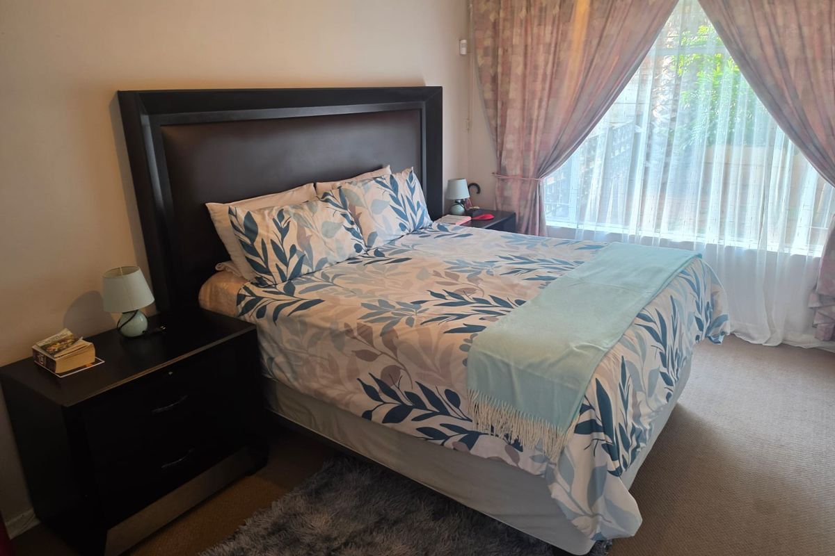 A comfortable bedroom featuring carpeted flooring and large windows with curtain treatments, providing a functional and well-lit sleeping space.