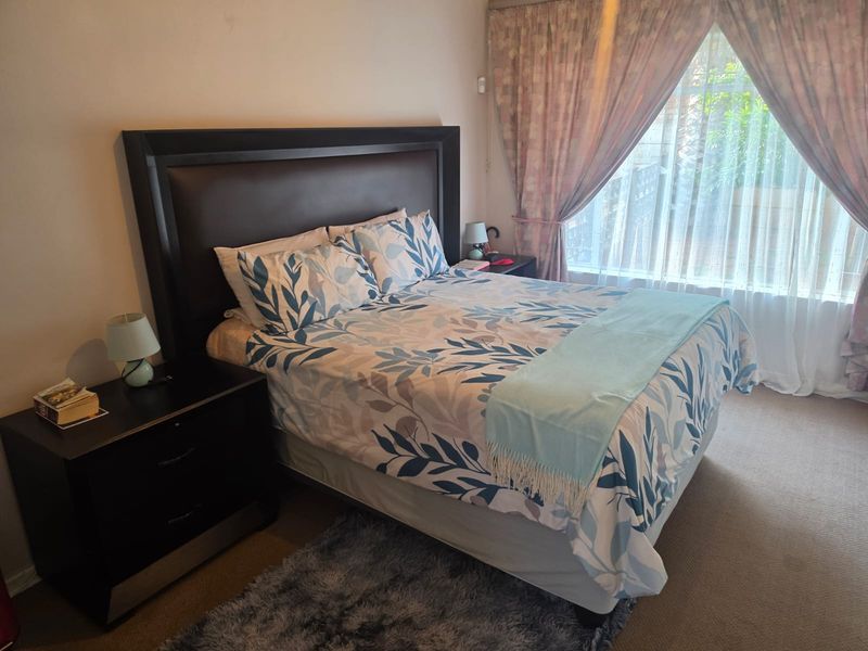 A comfortable bedroom featuring carpeted flooring and large windows with curtain treatments, providing a functional and well-lit sleeping space.
