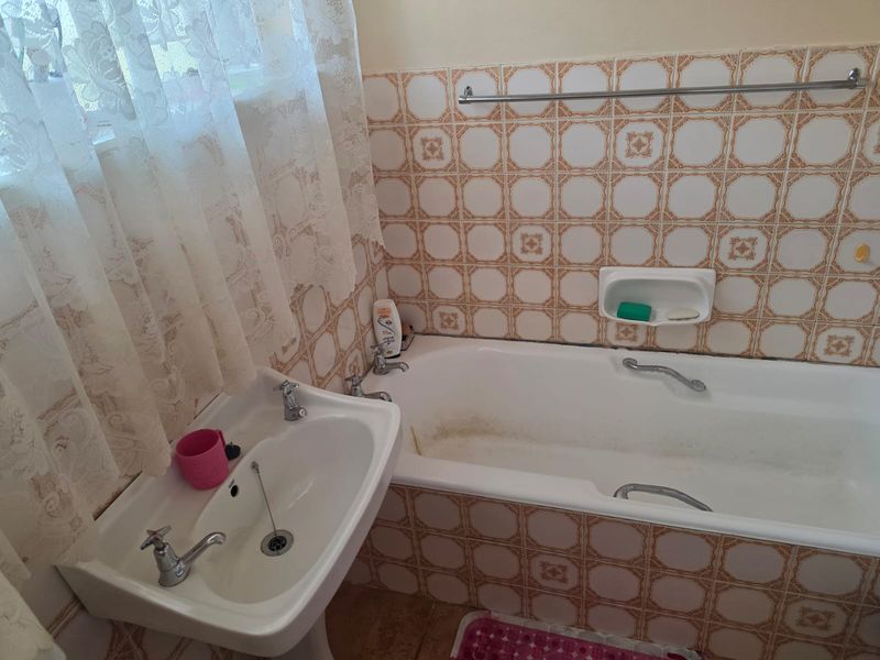A dated bathroom featuring a pedestal basin and a bathtub with decorative wall tiling and integrated soap dish.
