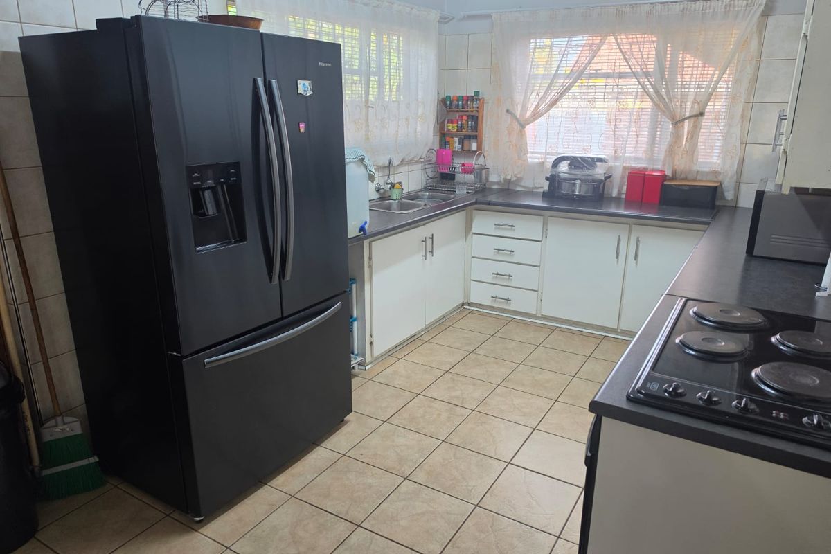 A functional kitchen featuring built-in cabinetry, laminate countertops, a double basin sink, and an electric hob with ceramic tile flooring.