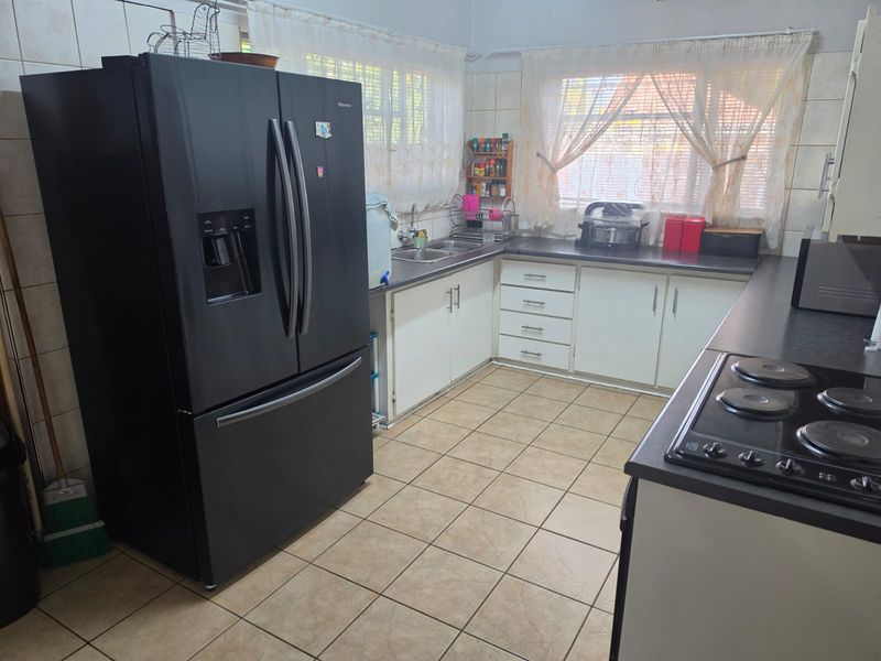 A functional kitchen featuring built-in cabinetry, laminate countertops, a double basin sink, and an electric hob with ceramic tile flooring.