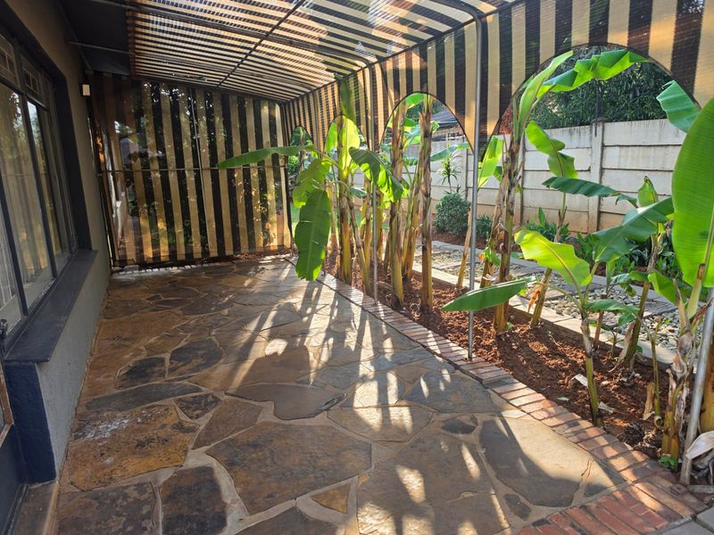 Covered patio area featuring flagstone paving, brick edging, and an arched shade structure, providing a sheltered outdoor space adjacent to the garden.