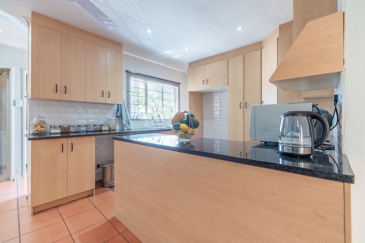 A functional kitchen featuring light wood cabinetry, black granite countertops, a subway tile backsplash, and terracotta floor tiles.