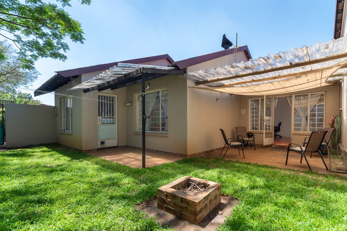 Rear exterior view of the townhouse featuring a paved patio area with a pergola, a brick fire pit, and a private garden space.
