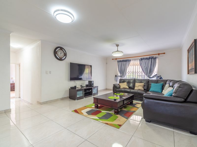 A spacious and bright living room featuring neutral tiled flooring, clean white walls, and a large window fitted with a security gate.