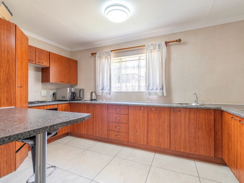 Functional kitchen featuring wood-finish cabinetry, granite countertops, tiled backsplash, and ceramic flooring, offering a practical layout for daily meal preparation.