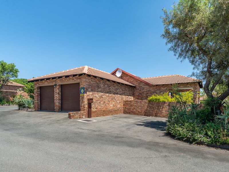 A well-maintained face-brick house featuring a double garage, tiled roof, and paved driveway, set within a landscaped residential environment.