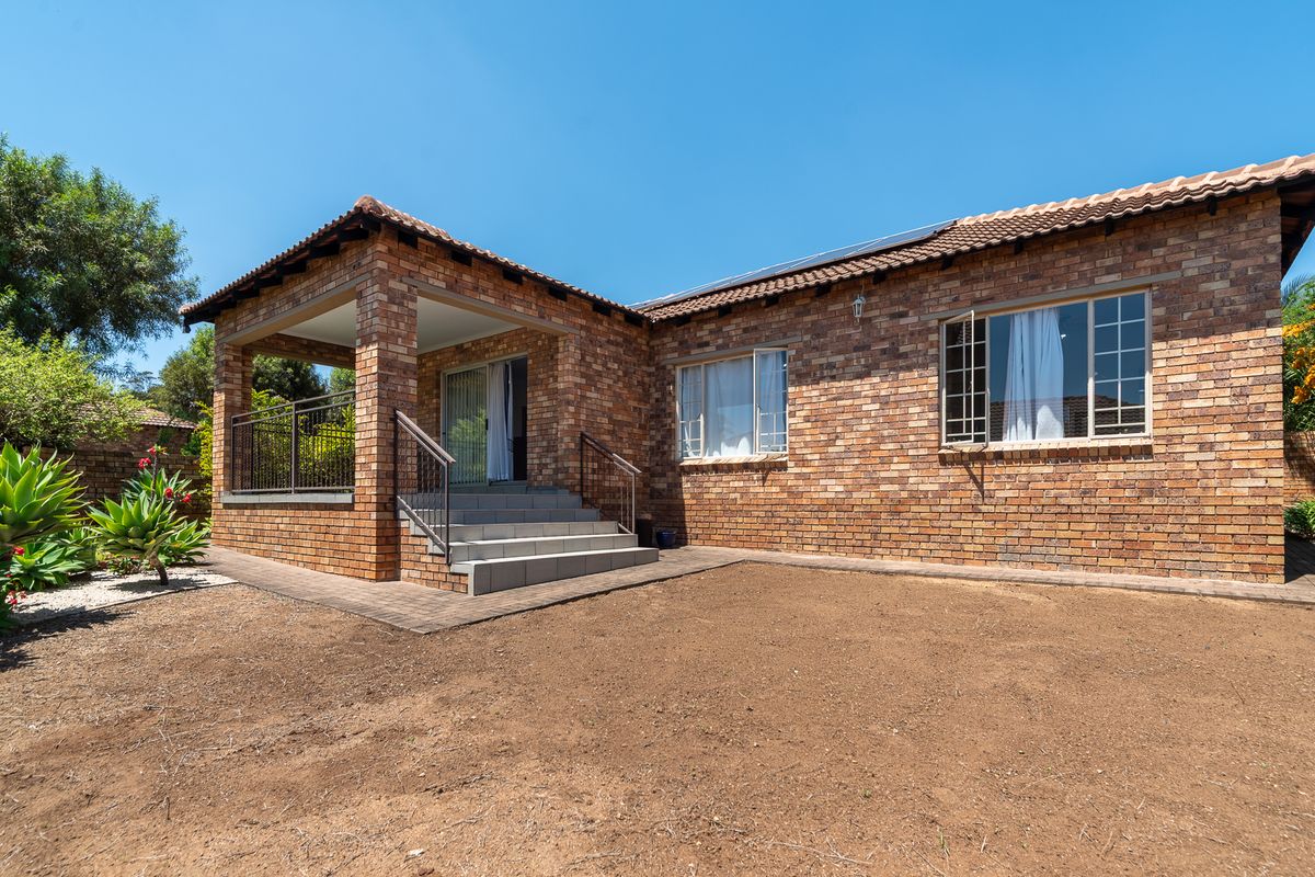 Rear view of a face brick house featuring a covered patio, tiled steps, and solar panels, set within a landscaped garden area.