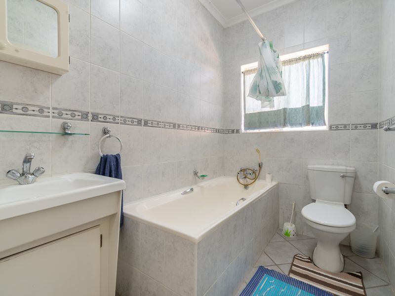 A functional bathroom featuring a built-in vanity, bathtub, and toilet with neutral wall tiling throughout.