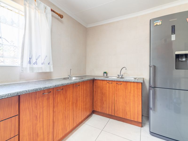 A functional scullery area featuring wood-look cabinetry, granite countertops, a double stainless steel sink, and neutral tiled finishes.