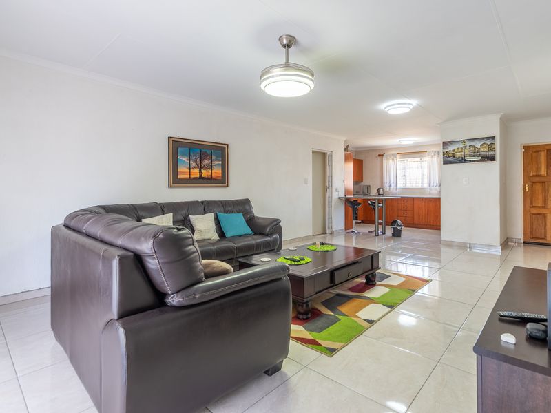 An open-plan living and kitchen area featuring tiled flooring, ceiling fans, and a functional kitchen with a breakfast bar.