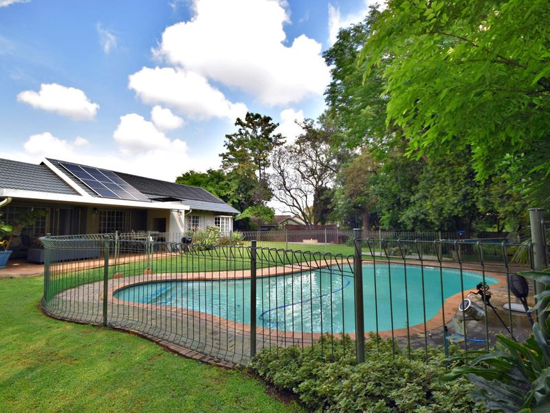 A well-maintained backyard featuring a swimming pool with a safety fence, a covered patio area, and solar panels installed on the house roof.