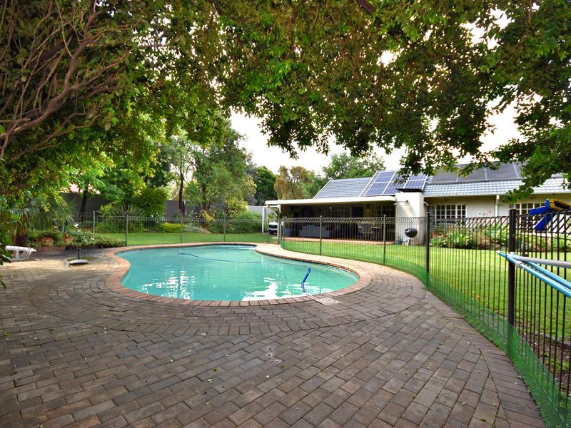 A well-maintained backyard featuring a swimming pool with brick paving, a safety fence, and a covered patio area with solar panels on the roof.