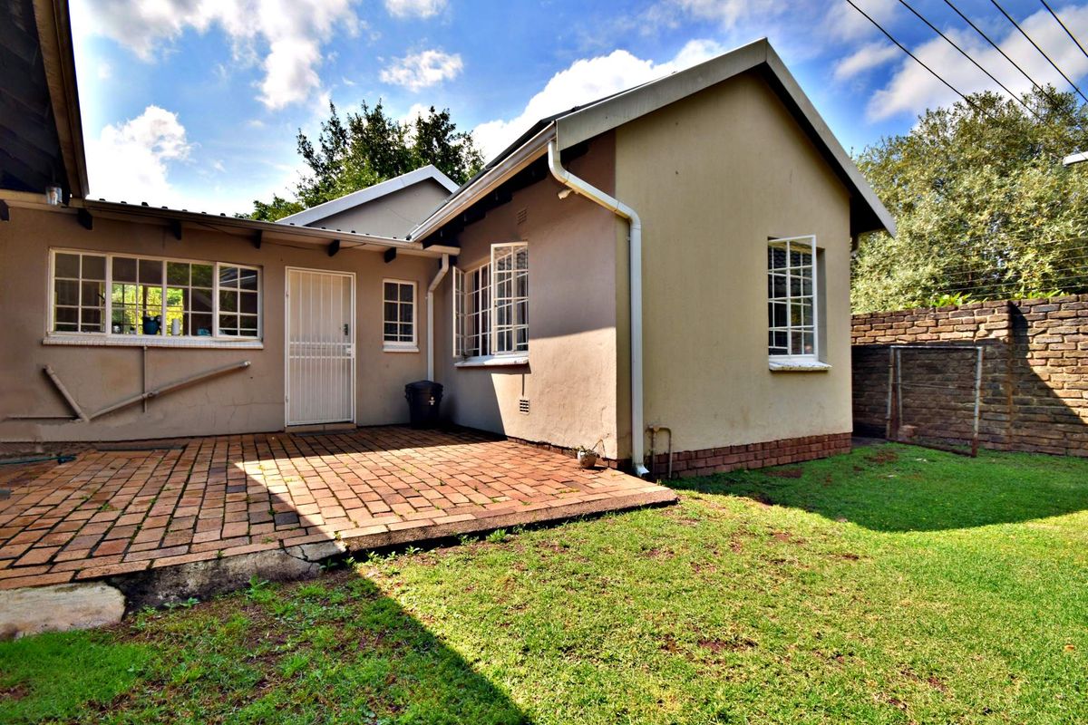 Rear view of the property featuring a brick-paved patio area, established garden, and secure steel-framed windows.