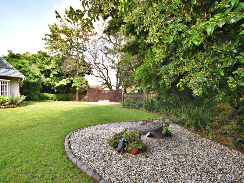 A well-maintained private garden featuring a lush lawn, mature trees, and a gravel-landscaped area with brick edging.