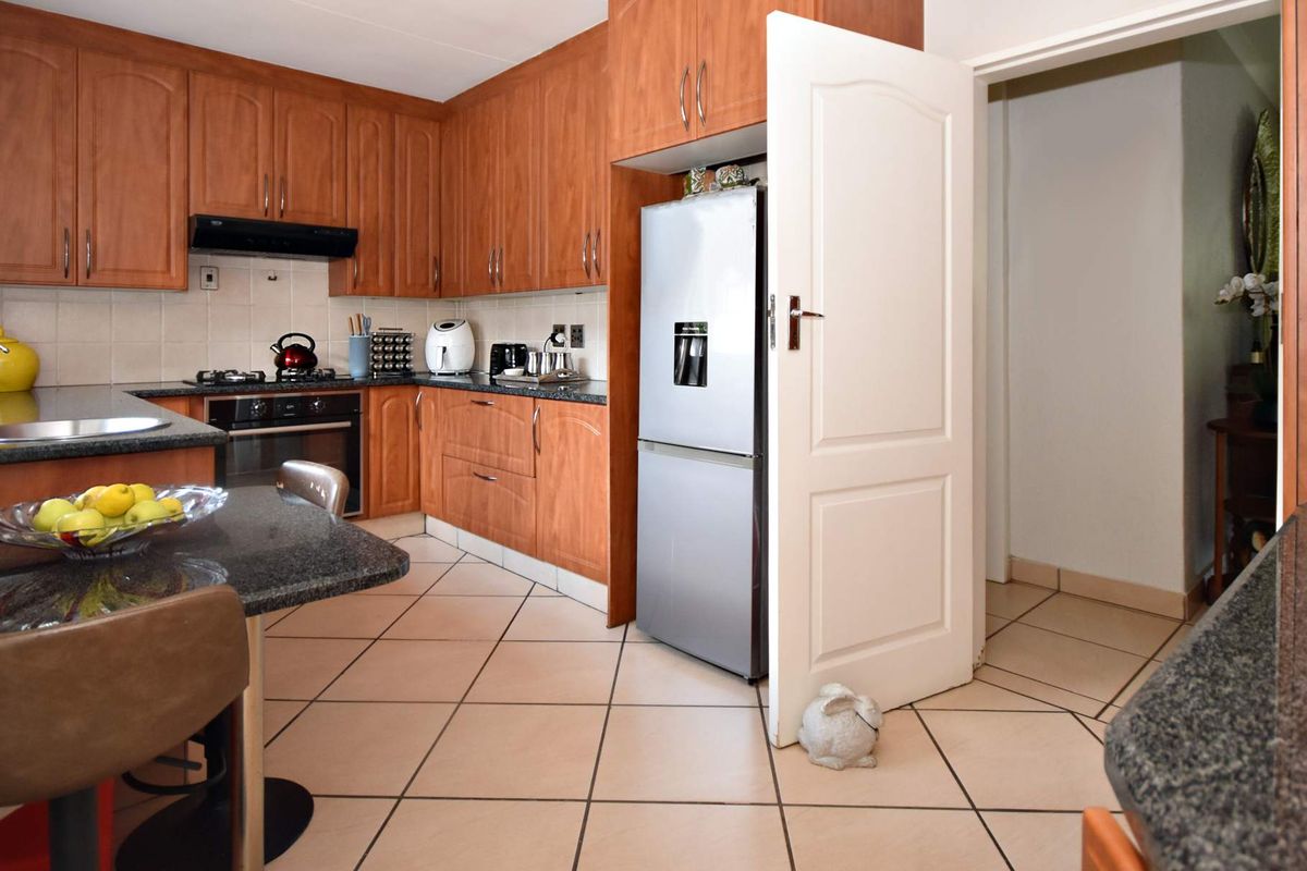 A functional kitchen featuring warm-toned wooden cabinetry, granite countertops, built-in oven, gas hob, and tiled flooring, offering a practical layout for daily cooking.
